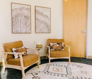TMS therapy waiting area with two mustard-colored chairs, small side table, and framed abstract wall art