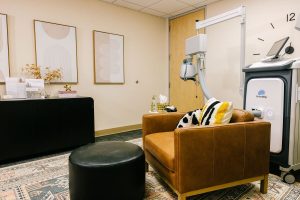 TMS treatment room with therapy couch, reception desk, BrainsWay TMS device, and framed artwork