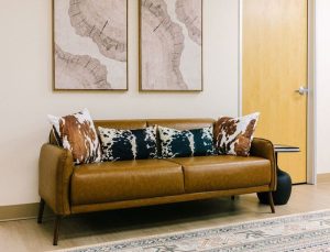 Caramel leather sofa with patterned pillows and framed abstract artwork above in a modern waiting room