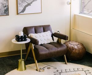 Brown leather chair with white pillow, brass side table, window view, and framed abstract map prints