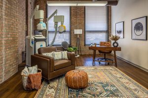 TMS treatment room with dental chair, overhead equipment, exposed brick, and modern furniture