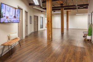 Spacious mental health clinic reception area with wood flooring, exposed wooden beams, benches, and TV screen on wall