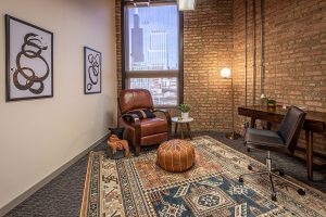Consultation room with two leather chairs facing each other, brick wall, city view window, and abstract line art on walls