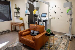 TMS therapy room with multiple treatment coils and a monitor, orange leather chair in foreground