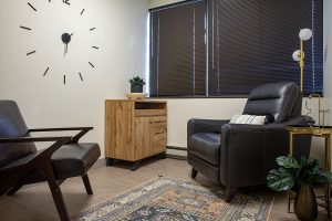 Private therapy office with two black leather recliners, wooden storage cabinet, and clock on wall