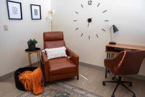 Quiet therapy room with brown leather recliner, desk, framed artwork, and geometric wall clock