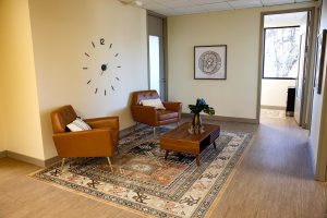 Waiting area with two brown leather armchairs, wooden table, plants, and wall clock
