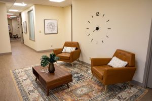 Modern waiting room with two brown leather chairs, wooden coffee table with plant, and wall clock at Relief Mental Health practice
