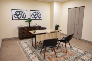 Office reception area with wooden desk, black chair, abstract wall art, and storage cabinets at Relief Mental Health