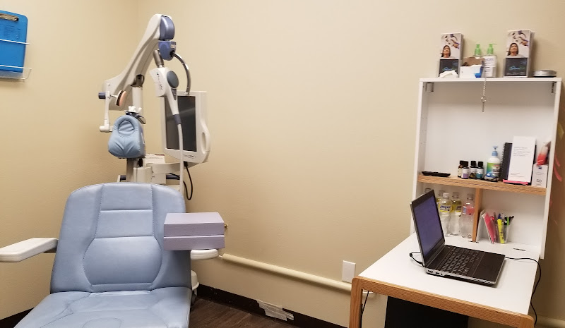 TMS therapy treatment room with patient chair, robotic TMS device arm positioned above, laptop workstation, and supply shelving