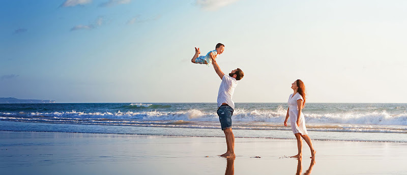 Family playing together on beach with young child held up by father while mother watches