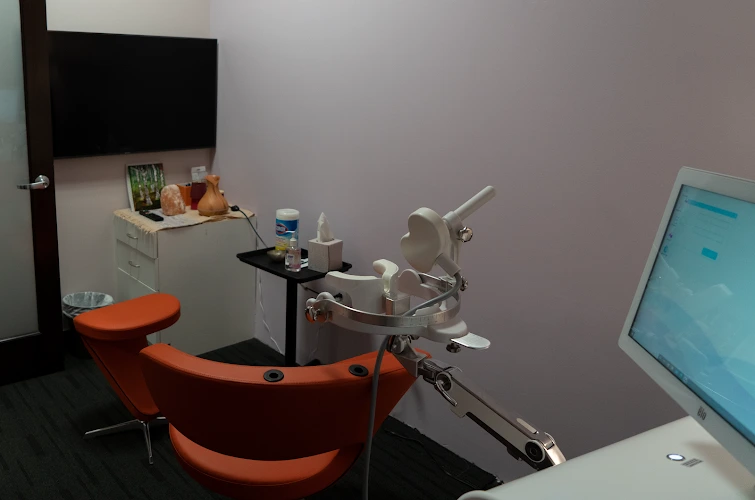 Rise TMS treatment room with orange patient chair, medical equipment, monitor, and control station