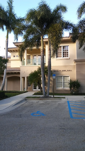 Two-story tan building with palm trees and blue handicap parking space in front