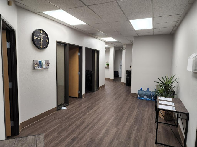 SAI Mental Health clinic hallway with multiple treatment room doors, wall clock, water bottles, and potted plant on side table
