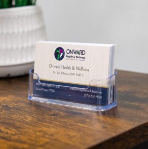 Onward Health & Wellness business cards in acrylic holder on wooden desk with white textured basket in background