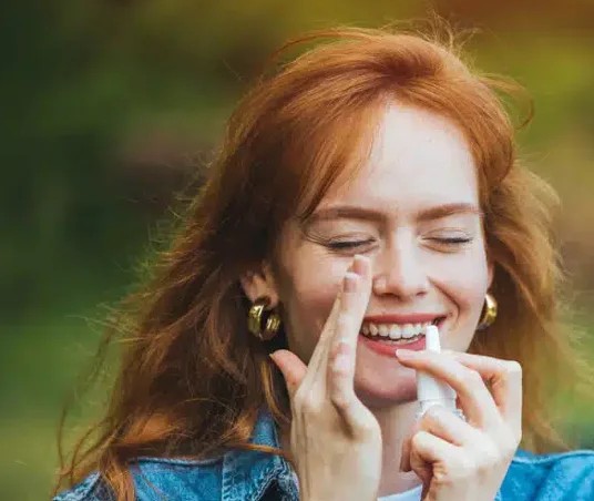 Woman applying lip balm outdoors with green blurred background