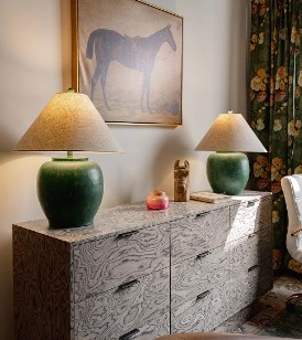 Marble dresser with two green ceramic table lamps and decorative items in a bright office setting