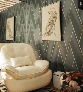 Cream-colored armchair against geometric patterned wall with framed botanical prints above