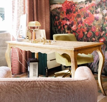 Light wood desk with green chair in office space featuring red floral artwork and striped curtains