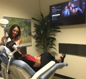 Clinician demonstrating TMS therapy to a patient in treatment chair with monitor displaying session in background