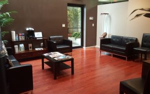 Modern medical office waiting room with red polished concrete floor, black leather seating, wooden cabinets, and glass doors opening to outdoor patio