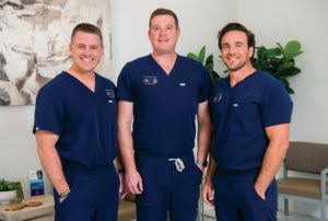 Three NeuroJust providers in navy scrubs standing together in clinical office setting