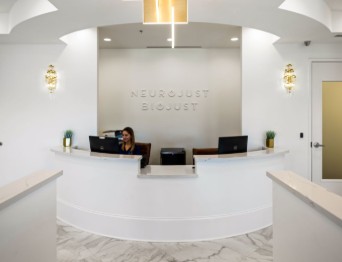 Neuroqüit Clinic reception desk with white curved counter, staff member, and modern lighting in bright clinical space