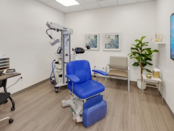 TMS therapy treatment room with blue chair, medical device on arm, desk, and plant in clinical setting