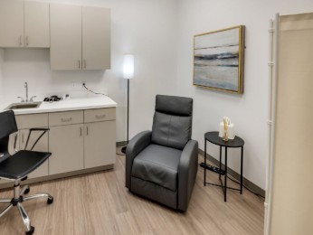 Clinical consultation room with sink cabinet, black reclining chair, lamp, and landscape artwork