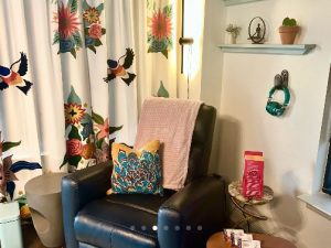 Welcoming therapy nook with blue armchair, botanical patterned curtains, and decorative wall shelving