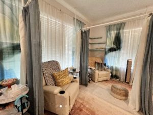 Treatment room with four-poster curtained canopy frame, comfortable seating, and neutral decor