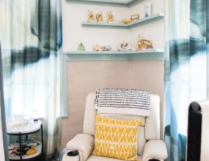 Cozy therapy alcove with cream armchair, yellow patterned pillow, floating shelves, and blue-gray curtains