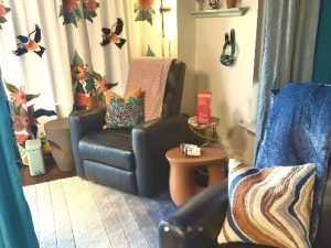 Therapy space with dark armchair, patterned curtains, wooden side table, and colorful throw pillows
