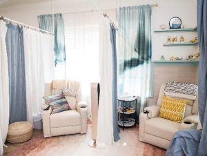 Calming therapy room with cream armchair, hanging blue curtains, wooden side table, and floating shelves with decor