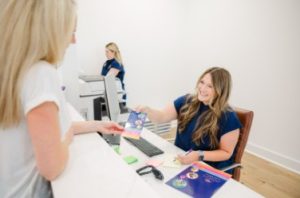 Receptionist handing purple intake form to patient at clinic check-in desk