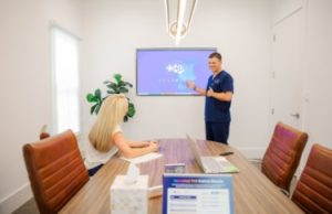 Clinician presenting brain scan on wall monitor to patient seated at conference table