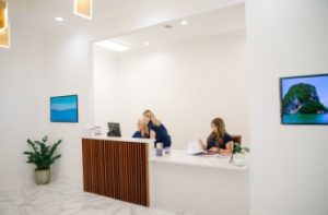 Reception desk with two staff members greeting patients in bright clinical space