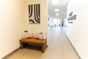 Medical office hallway with a tan leather bench, striped wall art, and glass-fronted office space
