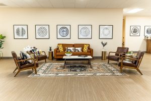 TMS therapy waiting area with brown leather seating, geometric wall art, patterned rugs, and wood tables