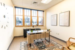 TMS therapy office with desk, windows overlooking bare trees, wall clock, and framed artwork