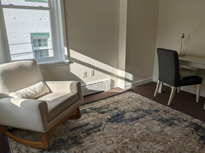 Bright therapy room with cream armchair, black chair, desk, and window with city view