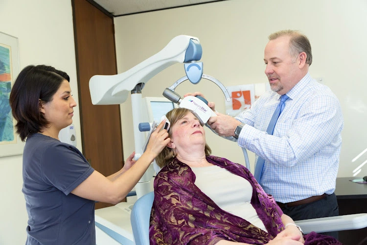 Clinician positioning TMS coil on patient's head while staff member observes during treatment