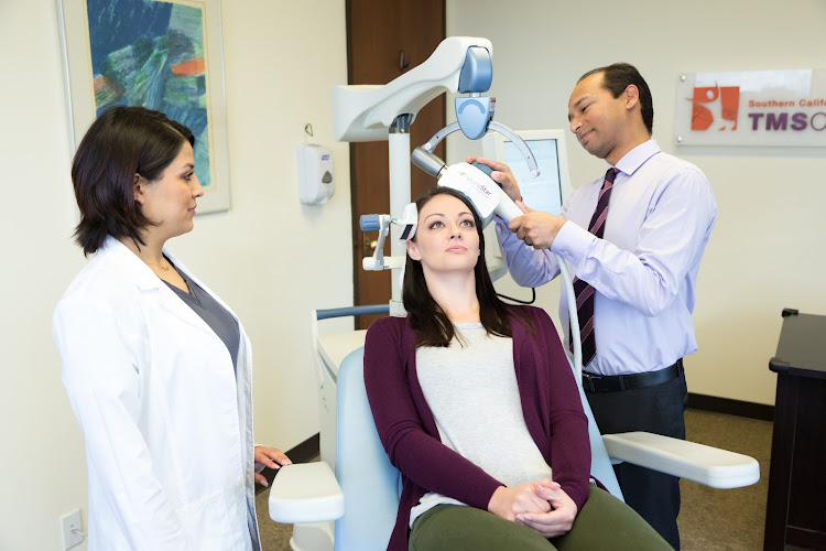 Two clinicians positioning TMS coil on seated patient's head during therapy session