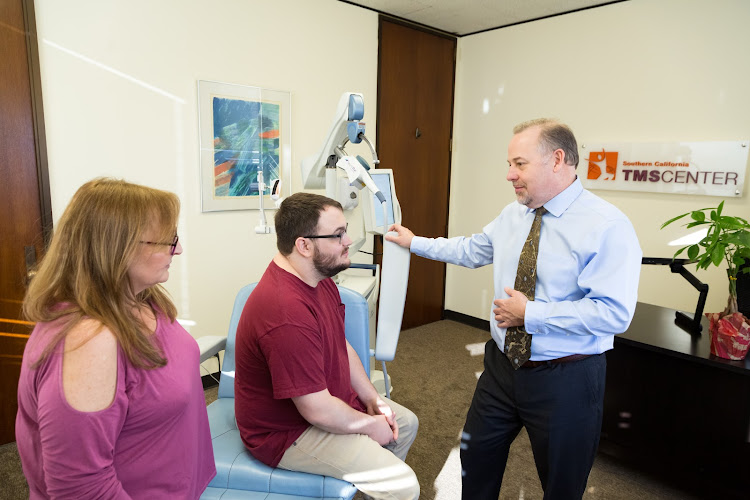 Male clinician explaining TMS device to two patients in Southern California TMS Center treatment room