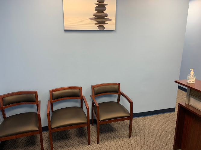 Healthcare waiting room with three wooden chairs, stacked stones artwork, and light gray walls