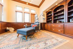 Comfortable waiting room with blue upholstered chair, ottoman, wooden shelving, and large windows