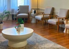 Stella clinic waiting room with mid-century wooden chairs, white round side table, potted plants, and large windows