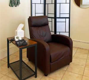 Private treatment room with brown reclining chair, side table with medical device, hanging plant, and room divider