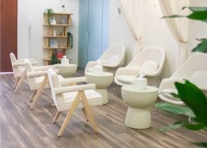 Modern TMS therapy waiting room with cream chairs, wooden shelving, potted plants, and blue cabinet doors