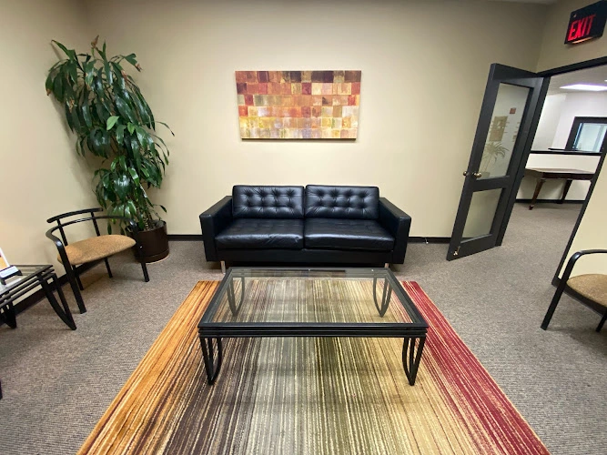 Telemind Clinic waiting area with black leather sofa, glass coffee table, colorful wall art, large potted plant, and exit sign